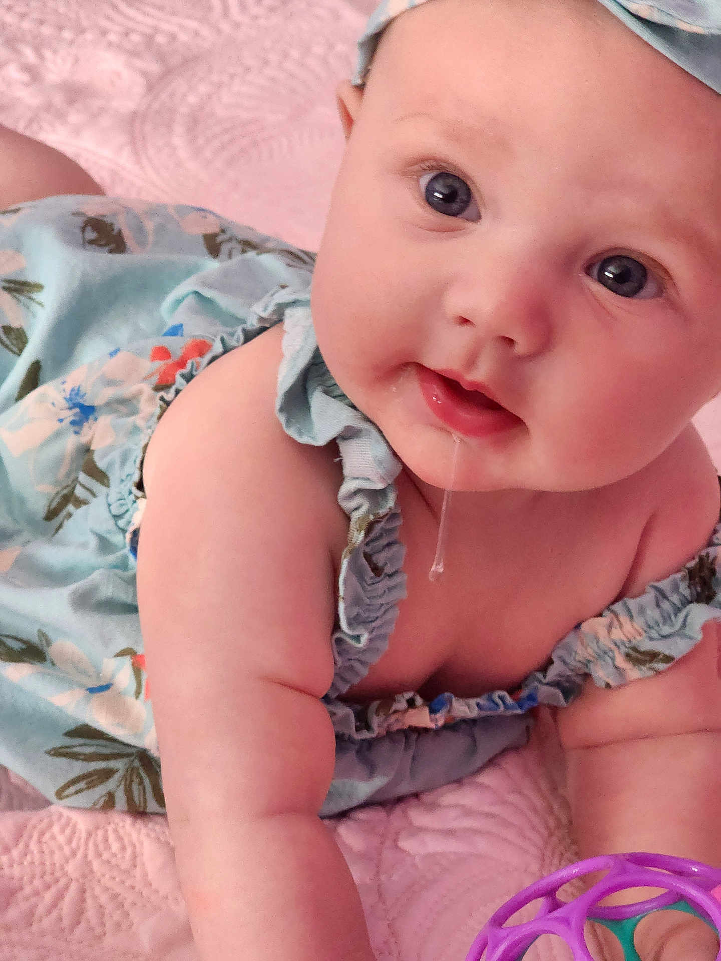 Hannah joined the competition — help win amazing prizes! baby, child, drool, blue_dress, headband, toy, purple_toy, teal_toy, pink_blanket, closeup, face, arms, skin, infant, cute, portrait, indoor, expression, eyes, chubby
