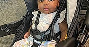 Zendaya is registered to the contest to win money with this photo: baby, child, stroller, bow, headband, clothing, floral, socks, straps, seat, carpet, indoor, infant, cute, baby_girl, person, portrait, comfortable, curious, smiling