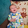 Leo joined the competition — help win amazing prizes! baby, smiling, onesie, couch, pillow, floral_pattern, happy, indoor, child, face, infant, seated, colorful_clothing, home, cute, comfortable, portrait, furniture, young_child, relaxed