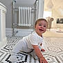 baby, child, crawling, smiling, floor, tile, hexagonal_tile, white_clothing, gray_clothing, sock, indoor, radiator, furniture, living_room, happy, person, cute, head, hand, home