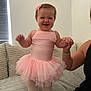Ivy is registered to the contest to win money with this photo: baby, child, tutu, pink_dress, smiling, happy, indoor, couch, holding_hand, person, cute, tights, toddler, woman_hand, home, portrait, fabric, light, furniture, blush
