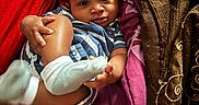 Drayce is registered to the contest to win money with this photo: baby, child, infant, portrait, sitting, lying_down, smiling, face, hands, feet, socks, striped_clothing, blanket, bed, indoor, cozy, colorful, red_clothing, brown_blanket, family