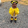 child, girl, outdoor, portrait, smiling, yellow_outfit, hair_bows, pigtails, cardigan, dress, ruffled_socks, black_shoes, standing, hands_on_cheeks, gravel, grass, playground, daylight, fashion, cute