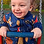 toddler, child, swing, playground, jacket, animal_print, hands, smile, curly_hair, outdoor, daylight, happy, metal_chains, blue, red, green_background, face, person, play, fun
