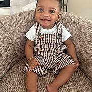 Jaxon joined the competition — help win amazing prizes! toddler, child, smile, happy, curly_hair, overalls, checkered, armchair, indoors, person, barefoot, bracelet, cute, portrait, seated, infant, clothing, furniture, baby, cheerful