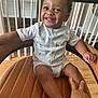 child, toddler, smiling, chair, leather, hand, baby_clothes, indoor, wood_floor, railing, window, natural_light, happy, person, cute, sitting, curly_hair, infant, home, portrait