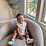 Jaxon is registered to the contest to win money with this photo: toddler, child, smiling, indoor, armchair, window, natural_light, plant, romper, sneakers, happy, cozy, carpet, home, person, portrait, furniture, bright, casual, cute