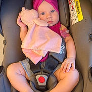 Ella a rejoint le concours — aidez-le/la à gagner de superbes lots ! baby, car_seat, plush_toy, headband, pacifier, pink, maroon, infant, child, sitting, safety_harness, indoor, cute, soft_toy, warning_label, airbag, clothing, person, legs, hand