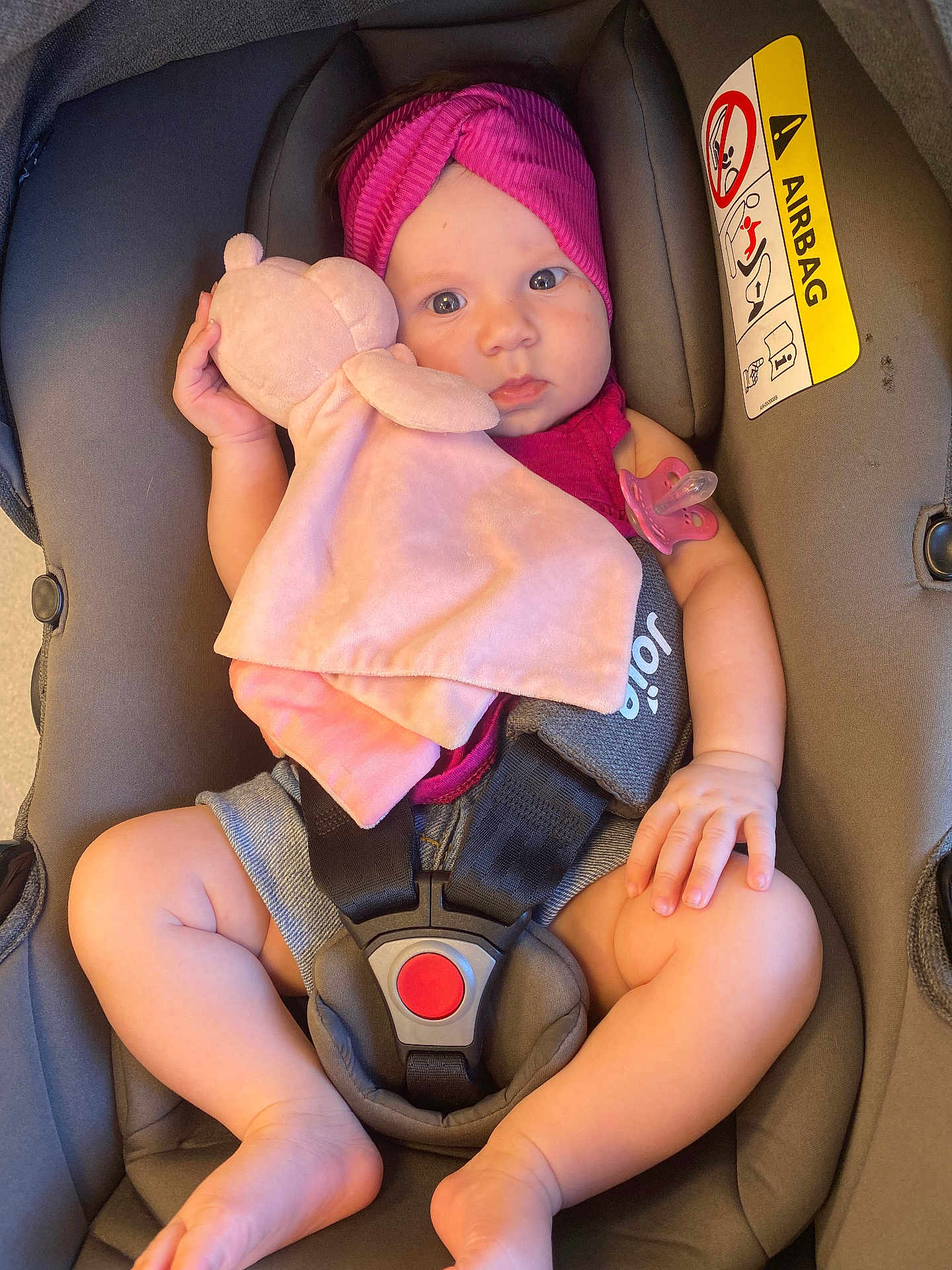 Ella a rejoint le concours — aidez-le/la à gagner de superbes lots ! baby, car_seat, plush_toy, headband, pacifier, pink, maroon, infant, child, sitting, safety_harness, indoor, cute, soft_toy, warning_label, airbag, clothing, person, legs, hand