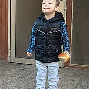 Patrick participe au concours pour gagner de l'argent avec cette photo : black_vest, blue_shoes, boy, casual_clothing, checkered_shirt, child, concrete_floor, door, footwear, hair, happy, light_pants, outdoor, person, playful, portrait, smiling, standing, toy, young