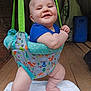 animal_pattern, baby, child, clothing, colorful, cute, drool, face, feet, green_straps, happy, indoor, infant, jumper, legs, person, smiling, suspend, white_towel, wooden_floor