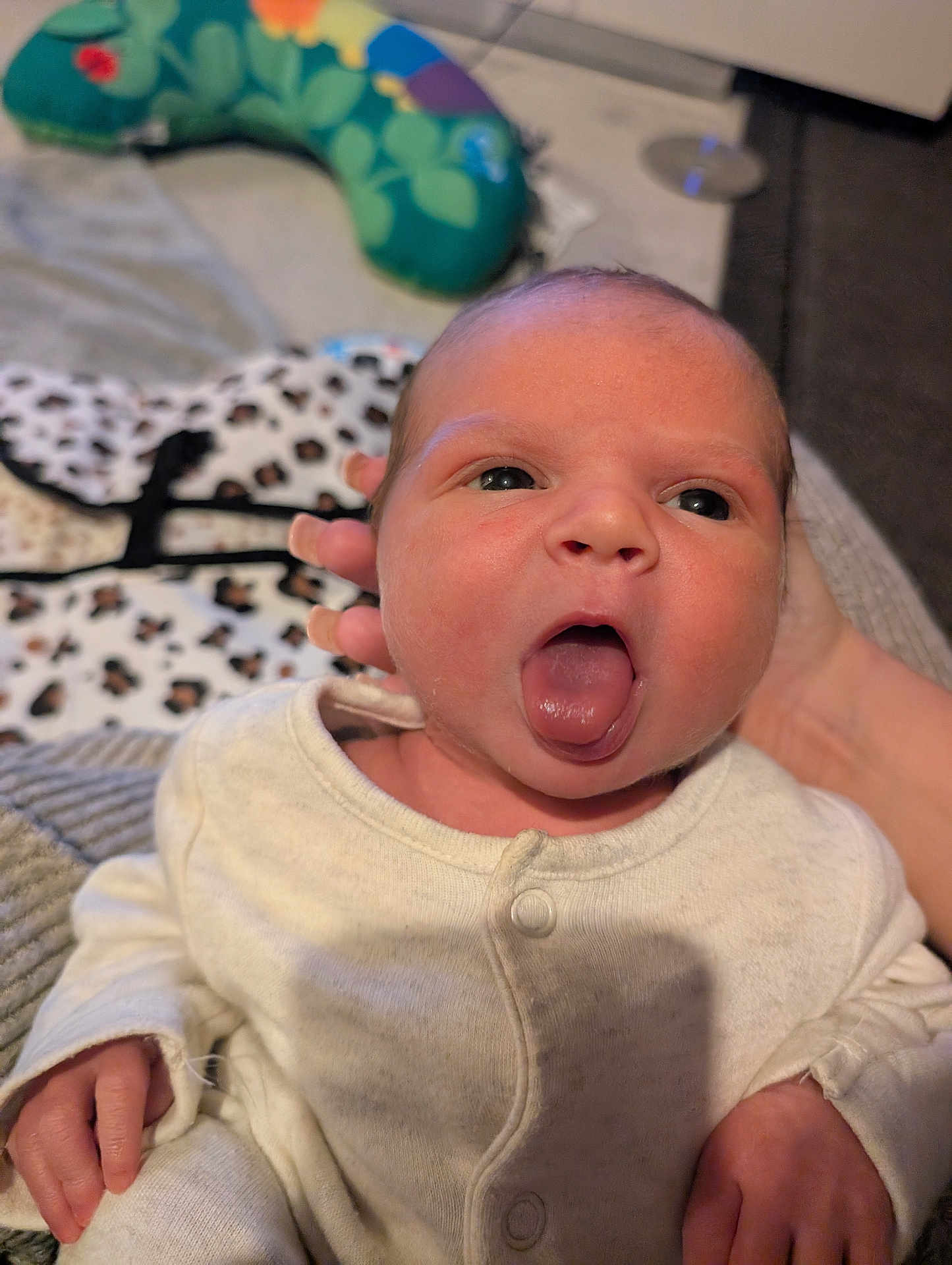 Zeniyah is registered to the contest to win money with this photo: newborn, baby, infant, face, tongue_out, onesie, hand, person, indoor, soft_toys, baby_pillow, expression, skin, cute, portrait, cozy, human, child, support, blurred_background