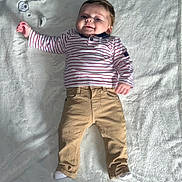 Soan a rejoint le concours — aidez-le/la à gagner de superbes lots ! baby, infant, child, smiling, striped_shirt, pants, white_blanket, lying_down, cute, happy, cozy, casual_clothing, indoor, portrait, young_child, small_child, one_arm_raised, soft_texture, comfortable, relaxed