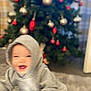 Elijah is registered to the contest to win money with this photo: baby, child, hoodie, gray_clothing, christmas_tree, ornaments, red_ornaments, gold_ornaments, indoor, carpet, holiday, blurred, motion_blur, smiling, festive, decorations, person, home, celebration, happy