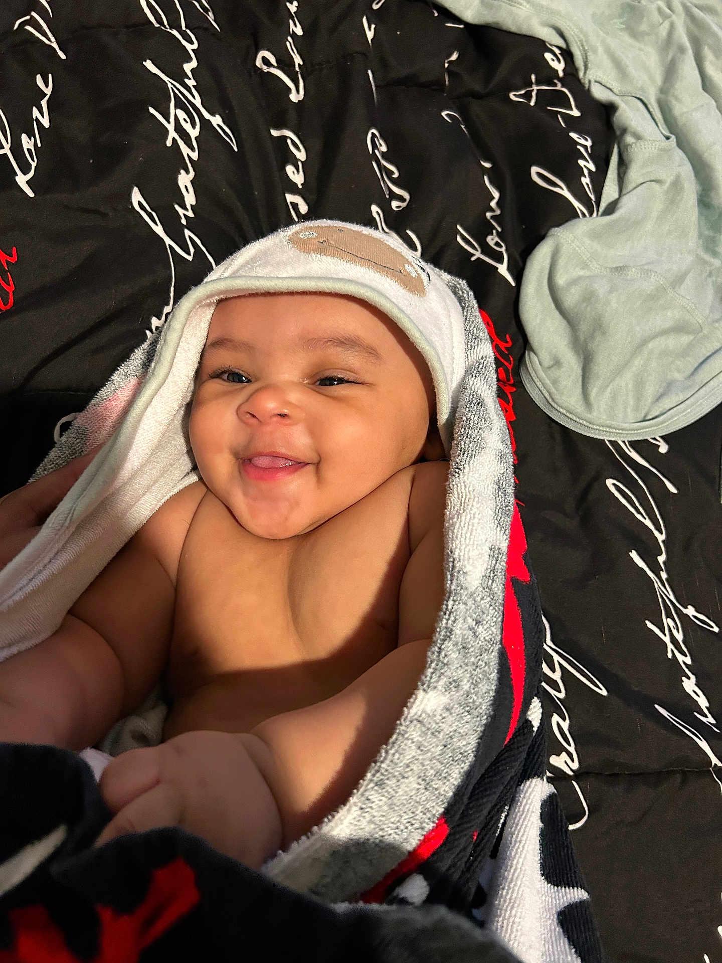 Jeremiah joined the competition — help win amazing prizes! baby, smiling, towel, hooded_towel, bed, blanket, text_pattern, happy, infant, cute, child, skin, face, hand, lying_down, comfort, indoors, soft, cozy, sleepwear