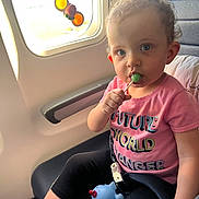 Adalynn joined the competition — help win amazing prizes! airplane_seat, black_leggings, blanket, blue_eyes, child, closeup, colorful_decorations, curly_hair, cute, indoor, lollipop, person, pink_shirt, seatbelt, sitting, snack, toddler, toy, travel, window