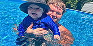 Easton joined the competition — help win amazing prizes! baby, child, adult, man, pool, water, swimming, hat, blue_clothing, smile, outdoor, sunny, summer, nature, greenery, happy, family, fun, recreation, leisure
