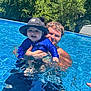 baby, child, adult, man, pool, water, swimming, hat, blue_clothing, smile, outdoor, sunny, summer, nature, greenery, happy, family, fun, recreation, leisure