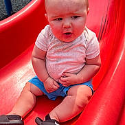 Easton joined the competition — help win amazing prizes! baby, child, slide, playground, outdoor, summer, footwear, nike, sandals, clothing, red_slide, curious_expression, sunlight, grass, shorts, shirt, person, legs, hands, baby_boy
