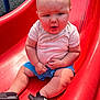 baby, child, slide, playground, outdoor, summer, footwear, nike, sandals, clothing, red_slide, curious_expression, sunlight, grass, shorts, shirt, person, legs, hands, baby_boy
