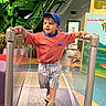 Levi joined the competition — help win amazing prizes! child, toddler, indoor, playground, treadmill, blue_cap, coral_tshirt, striped_shorts, gray_shoes, handrails, smiling, walking, educational_display, green_machine, play_area, person, floor, bench, reflection, museum