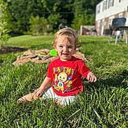 Greyson is registered to the contest to win money with this photo: toddler, child, grass, outdoor, sunlight, red_tshirt, playtime, smiling, sitting, backyard, greenery, daytime, person, young_child, happy, shorts, nature, casual, cute, portrait