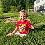 toddler, child, grass, outdoor, sunlight, red_tshirt, playtime, smiling, sitting, backyard, greenery, daytime, person, young_child, happy, shorts, nature, casual, cute, portrait