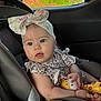 Melania is registered to the contest to win money with this photo: baby, child, car_seat, headband, toy, giraffe_toy, blue_eyes, floral_dress, seatbelt, infant, cute, indoors, car_interior, sitting, portrait, child_toy, expression, soft_light, closeup, curious