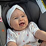 baby, infant, smiling, happy, car_seat, headband, white_outfit, cute, blue_eyes, child, portrait, indoors, soft_light, young, joyful, person, apparel, sitting, closeup, cute_expression