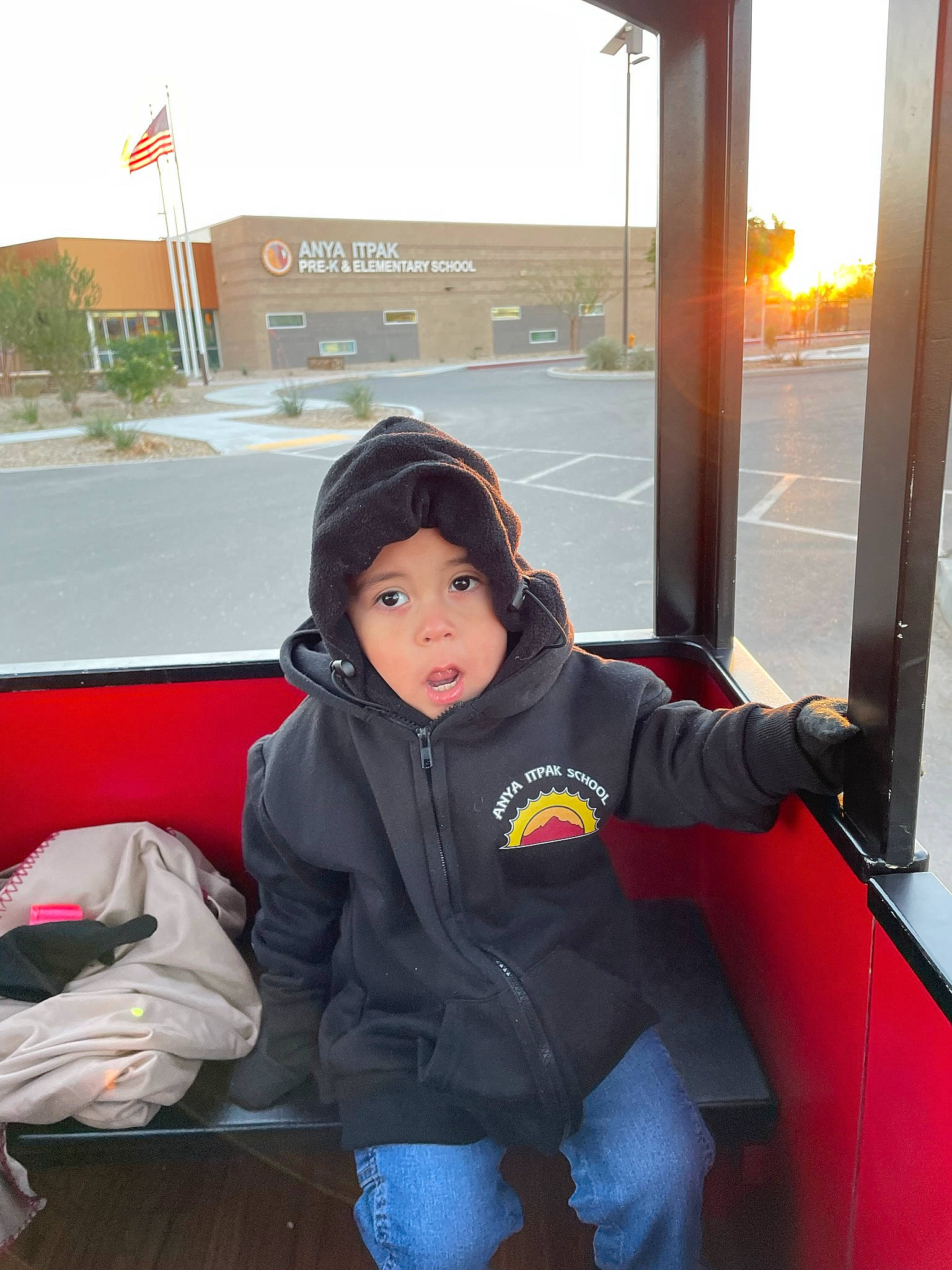 Gabe is registered to the contest to win money with this photo: backpack, bag, child, comfort, flag, fun, headwear, hoodie, jacket, leisure, luggage_and_bags, luxury_vehicle, passenger, person, personal_protective_equipment, public_transport, recreation, sitting, toddler, travel