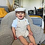 Louis a rejoint le concours — aidez-le/la à gagner de superbes lots ! toddler, child, smiling, armchair, overalls, cap, living_room, cushion, furniture, decor, plant, wooden_floor, table, chair, happy, person, indoors, portrait, casual_clothing, cute