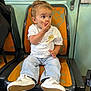 toddler, child, seat, orange_seat, white_tshirt, jeans, sneakers, hand_on_mouth, surprised_expression, public_transport, window, green_wall, indoor, person, young_child, casual_clothing, seat_back, curly_hair, footwear, sitting