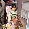 toddler, child, indoor, pink_chair, fluffy, toy, shelf, person, adult, pants, sweater, shoes, floor, light, hair, face, expression, furniture, room, curious