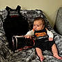 Daniel is registered to the contest to win money with this photo: baby, infant, child, harley_davidson, onesie, overalls, toy_box, toy_motorcycle, wrench, fur_blanket, blanket, sitting, indoor, couch, portrait, face, hand, feet, clothing, wall