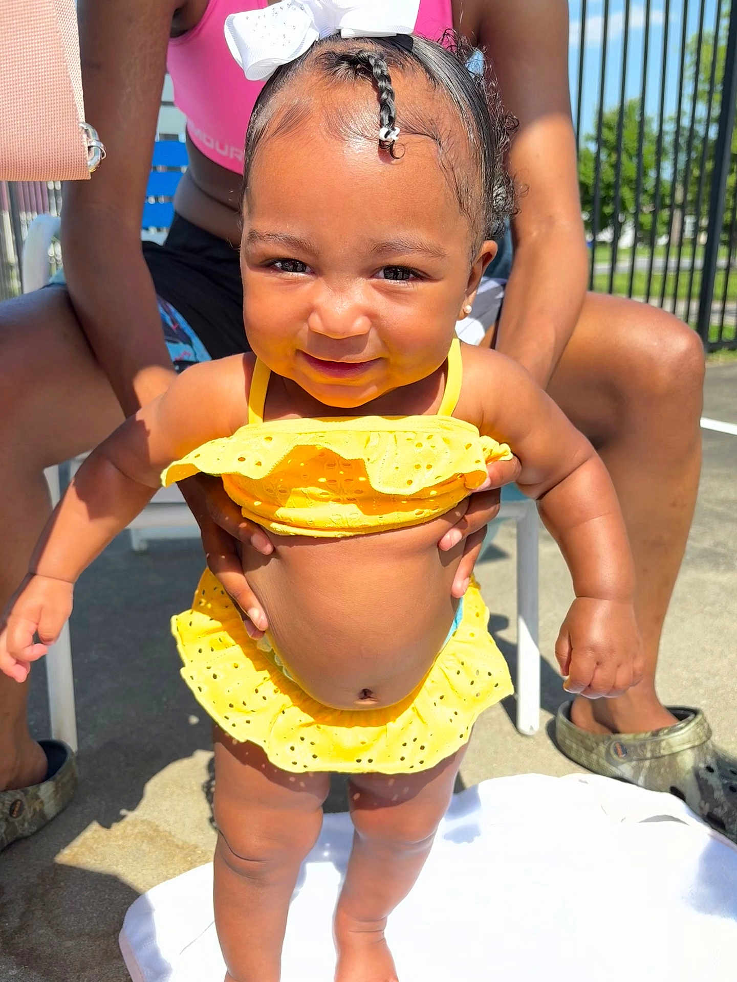Autumn joined the competition — help win amazing prizes! toddler, child, yellow_swimsuit, bow, smiling, outdoor, sunny, person, standing, baby, holding_hands, hair_bow, summer, happy, skin, legs, arms, adult_hands, concrete, footwear