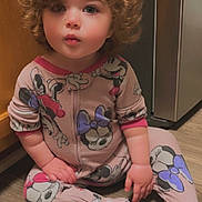 Everleigh is registered to the contest to win money with this photo: appliance, cabinet, child, curious, curly_hair, cute, expression, face, footwear, hands, indoor, kitchen, minnie_mouse, onesie, pajamas, patterned_clothing, pink, sitting, toddler, wood_floor