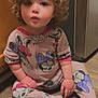 Everleigh is registered to the contest to win money with this photo: appliance, cabinet, child, curious, curly_hair, cute, expression, face, footwear, hands, indoor, kitchen, minnie_mouse, onesie, pajamas, patterned_clothing, pink, sitting, toddler, wood_floor