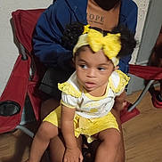 Jream is registered to the contest to win money with this photo: toddler, child, adult, yellow_clothing, headband, bow, sitting, lap, chair, indoor, wooden_floor, blue_hoodie, red_chair, person, curly_hair, casual, portrait, cozy, family, candid