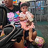 child, toddler, woman, indoor, bottle, pink_clothing, headband, curly_hair, sitting, chairs, play_area, carpet, sneakers, bag, holding, person, expression, casual_clothing, floor, stroller