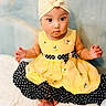 baby, child, dress, yellow, black, polka_dot, headband, flower, bee, sitting, feet, curious, cute, indoors, portrait, soft_background, fluffy, skin, hands, infant