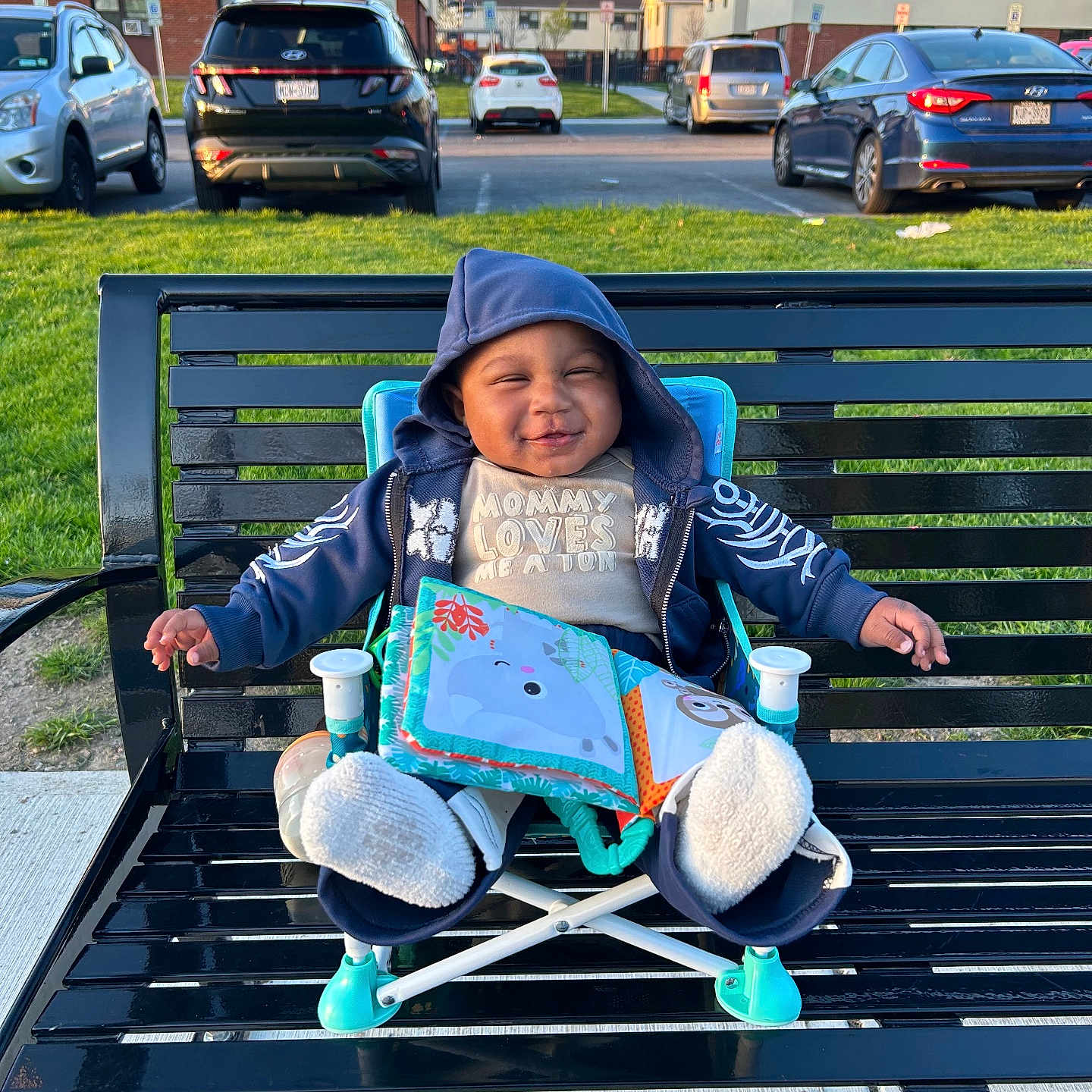 Ky joined the competition — help win amazing prizes! baby, bench, book, car, child, daylight, footwear, grass, happy, hoodie, jacket, outdoor, park, parking_lot, person, residential_building, seat, smile, suburb, toy