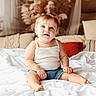 toddler, child, baby, sitting, bed, white_bedspread, blue_eyes, tank_top, denim_shorts, indoor, pillows, cozy, decor, home, portrait, cute, smiling, blond_hair, soft_light, relaxed