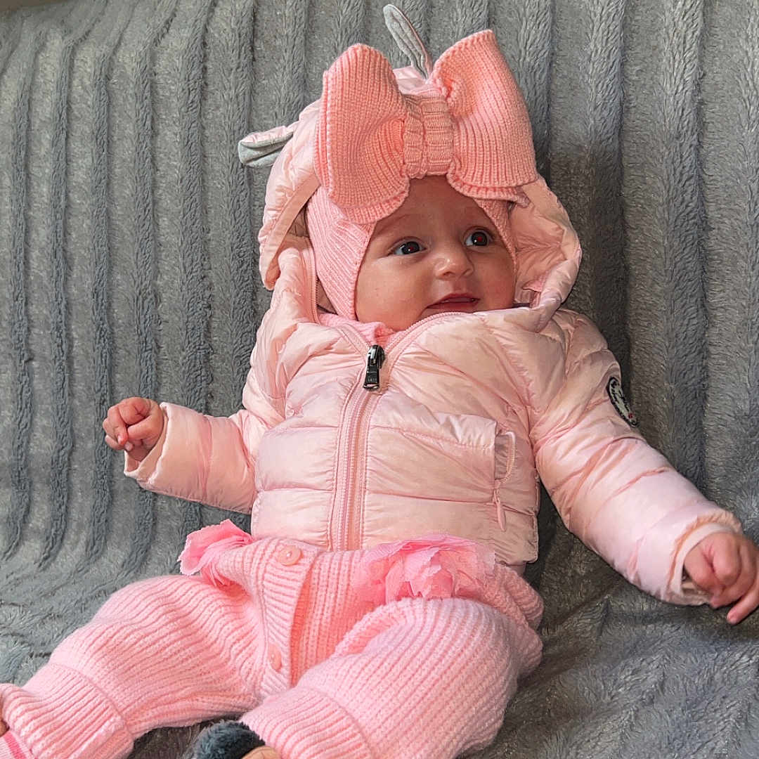 Zinaya a rejoint le concours — aidez-le/la à gagner de superbes lots ! apparel, baby, blanket, bow_hat, child, cozy, cute, happy, indoor, infant, jacket, knitwear, minnie_mouse, pink_clothing, portrait, seated, slippers, smiling, soft_texture, warm_clothes