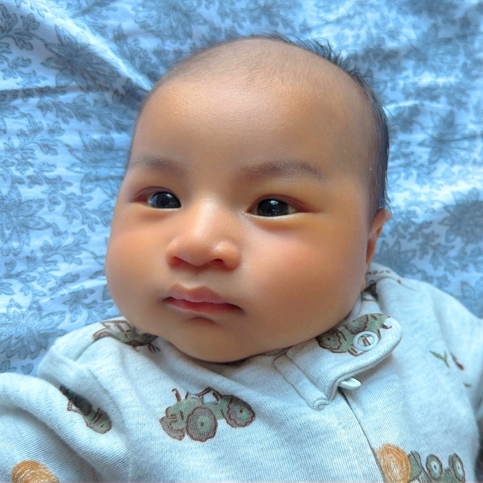 Peter Nguyen is registered to the contest to win money with this photo: baby, blanket, blue, cheeks, child, closeup, clothing, cute, eyes, face, indoors, infant, lying_down, onesie, pattern, portrait, skin, sleepwear, soft, young