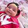 Nova is registered to the contest to win money with this photo: baby, child, hoodie, pink_bow, curly_hair, blanket, cartoon_pattern, smile, face, infant, clothing, lying_down, soft_texture, cute, indoors, portrait, head, red_clothing, happy, young_child