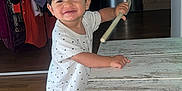 Sohan participe au concours pour gagner de l'argent avec cette photo : toddler, child, indoor, wooden_floor, polka_dot_clothing, barefoot, table, stick, smiling, happy, person, furniture, clothes, home, room, young_child, standing, wood, cute, playful