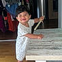 toddler, child, indoor, wooden_floor, polka_dot_clothing, barefoot, table, stick, smiling, happy, person, furniture, clothes, home, room, young_child, standing, wood, cute, playful