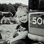 Camry joined the competition — help win amazing prizes! child, smiling, girl, curly_hair, bow, construction_vehicle, black_and_white, outdoor, jeans, tshirt, happy, portrait, sitting, vehicle, metal, rustic, playful, young, casual, cute