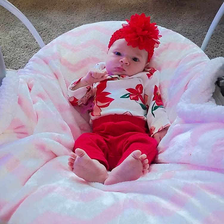 Johnna joined the competition — help win amazing prizes! baby, blanket, carpet, child, cozy, cute, floral_pattern, flower, foot, furniture, hand, headband, indoor, infant, person, portrait, red_clothing, resting, soft_texture, toddler