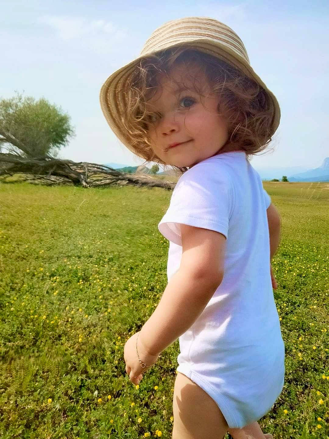 Mia participe au concours pour gagner de l'argent avec cette photo : face, grass, grassland, hair, hairstyle, happy, hat, head, leisure, natural_environment, people_in_nature, person, plant, shorts, skin, sky, standing, sun_hat, sunlight, toddler